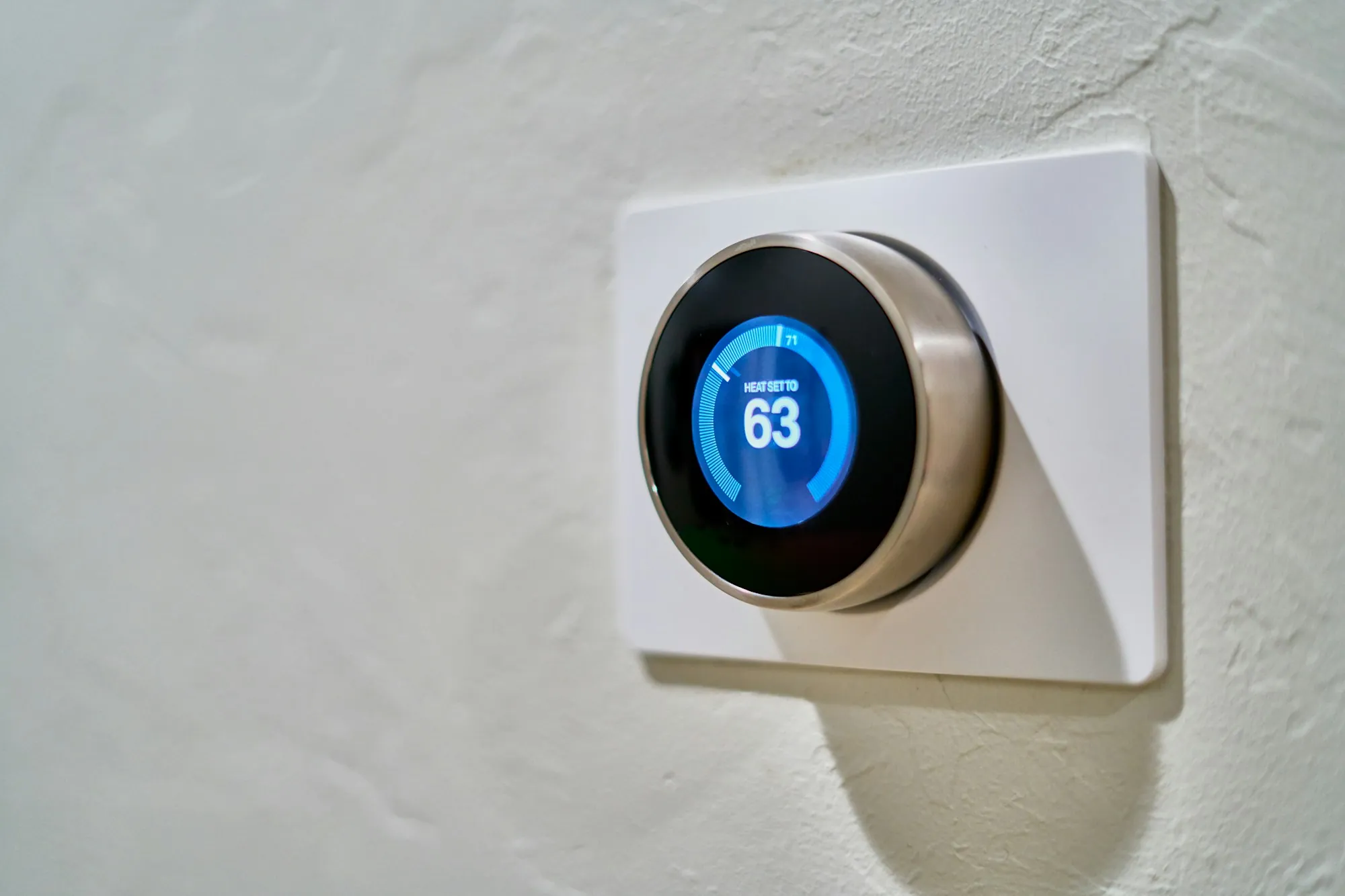 Round smart thermostat on a white wall showing 63 degrees