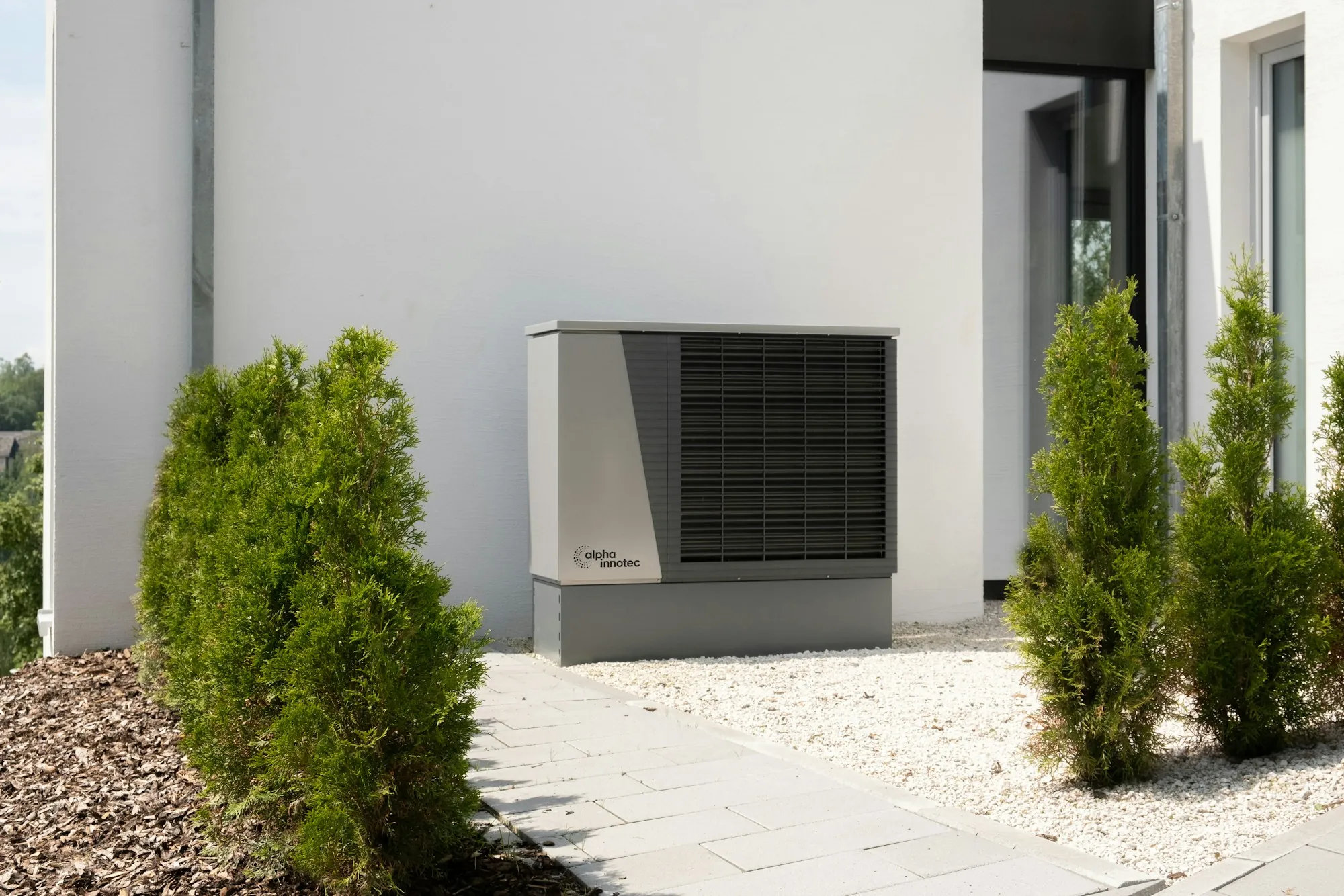 Heat pump unit outside a white home framed by shrubs